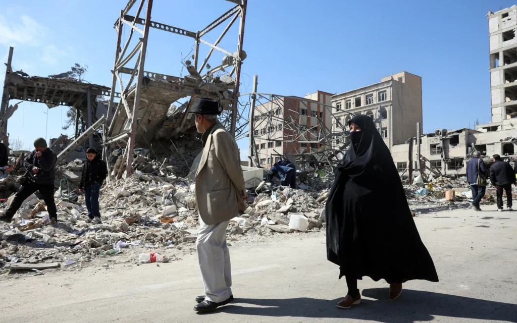 Un homme et une femme passent devant des bâtiments détruits par des frappes aériennes dans le centre de Téhéran, le 4 mars 2026. (Crédit: AFP)