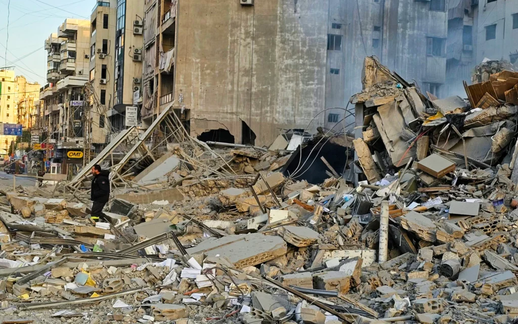 Un homme marche parmi les décombres d'un immeuble sur le site des frappes aériennes israéliennes de la nuit du 6 mars 2026 dans la banlieue sud de Beyrouth. (Crédit : AFP)