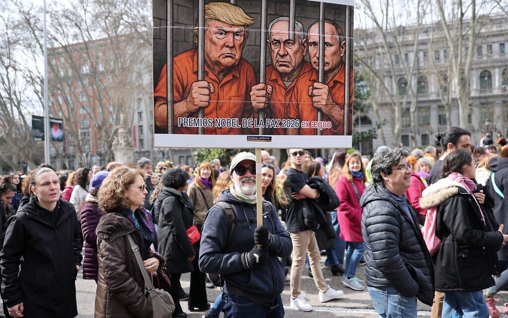 Un homme brandit une banderole se moquant du président américain Donald Trump, du Premier ministre Benjamin Netanyahu et du président russe Vladimir Poutine lors d'une manifestation marquant la Journée internationale des femmes à Madrid, le 8 mars 2026. (Crédit : Thomas COEX / AFP)