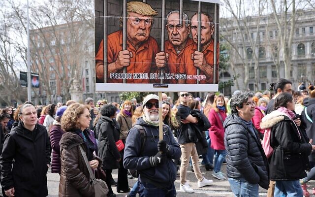 Un homme brandit une banderole se moquant du président américain Donald Trump, du Premier ministre Benjamin Netanyahu et du président russe Vladimir Poutine lors d'une manifestation marquant la Journée internationale des femmes à Madrid, le 8 mars 2026. (Crédit : Thomas COEX / AFP)
