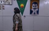 Une combattante kurde appartenant à la faction armée kurde iranienne Parti pour une vie libre au Kurdistan (PJAK) passe devant une affiche d'Abdullah Öcalan, fondateur emprisonné du Parti des travailleurs du Kurdistan (PKK), près de la frontière irako-iranienne, dans la région autonome du Kurdistan irakien, le 8 mars 2026. (Crédit : AFP)