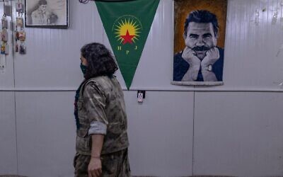 Une combattante kurde appartenant à la faction armée kurde iranienne Parti pour une vie libre au Kurdistan (PJAK) passe devant une affiche d'Abdullah Öcalan, fondateur emprisonné du Parti des travailleurs du Kurdistan (PKK), près de la frontière irako-iranienne, dans la région autonome du Kurdistan irakien, le 8 mars 2026. (Crédit : AFP)