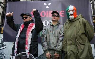 Liam O'Hanna (à gauche), qui se produit sous le nom de scène Mo Chara avec le groupe anti-Israël de punk-rap Kneecap, célèbre lors d'une conférence de presse avec ses camarades Naoise Ó Cairealláin (au centre), connu sous le nom de Moglai Bap, et JJ O Dochartaigh (à droite), connu sous le nom de DJ Provaí, au Conway Mill à Belfast, le 11 mars 2026. Liam O'Hanna, le chanteur irlandais du groupe punk-rap Kneecap, ne sera pas poursuivi pour terrorisme après que les procureurs britanniques ont perdu, le 11 mars, leur recours devant la Haute Cour contre la décision d'un juge de classer l'affaire. (Crédit : Paul Faith/AFP)