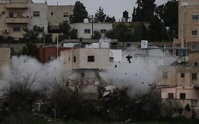 De la fumée et de la poussière s'élevant alors que l'armée israélienne détruit la maison d'Azmi Nader Abu Halill, impliqué dans une fusillade meurtrière en 2024, dans la ville de Dura, au sud de la Cisjordanie, le 14 mars 2026. (Crédit : Hazem Bader/AFP)