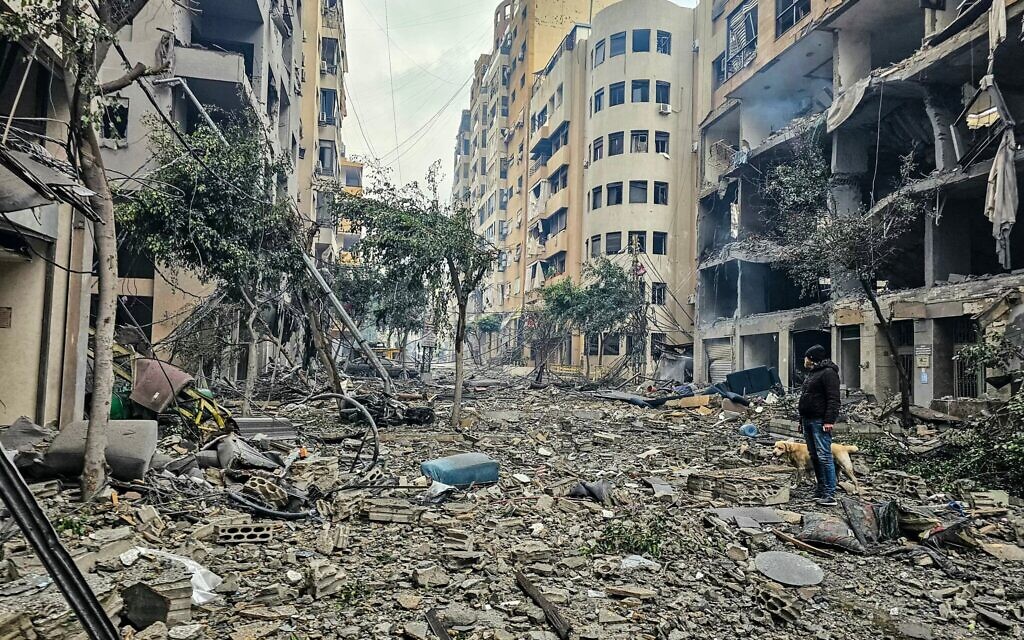Un homme et son chien marchant parmi les décombres d'un bâtiment sur le site d'une frappe aérienne israélienne, dans la banlieue sud de Beyrouth, à Haret Hreik, le 15 mars 2026. (Crédit : AFP)