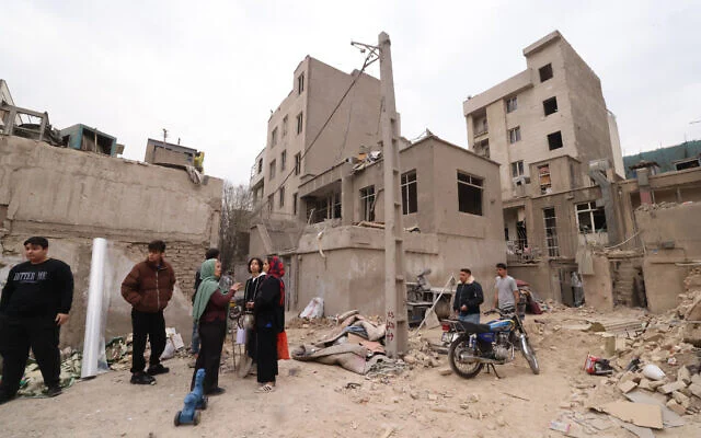 Des Iraniens se rassemblent devant des bâtiments détruits suite à une frappe militaire sur Téhéran,  la capitale de l'Iran, le 15 mars 2026. (Atta KENARE / AFP)