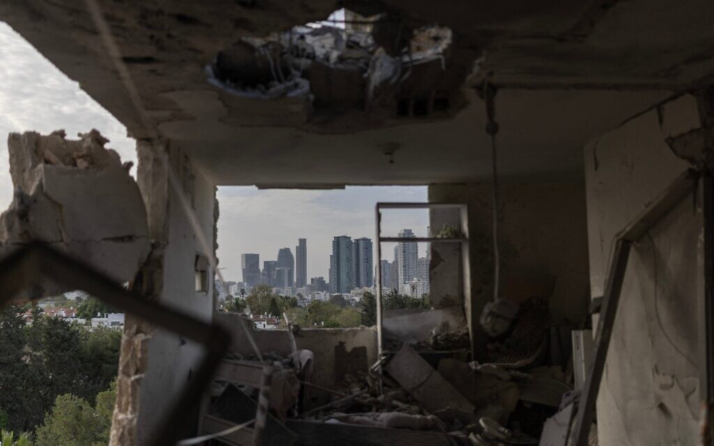 Cette photo montre l'intérieur d'un appartement détruit, avec la ligne d'horizon de Tel Aviv visible en arrière-plan, à la suite d'une frappe de missiles iraniens survenue dans la nuit du 19 mars 2026 (Crédit : Ilia YEFIMOVICH / AFP)