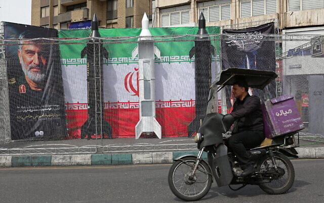 Un automobiliste passant devant des maquettes de missiles iraniens installées le long de la route près de la place Valiasr, à Téhéran, en Iran, le 22 mars 2026. (Crédit : AFP)
