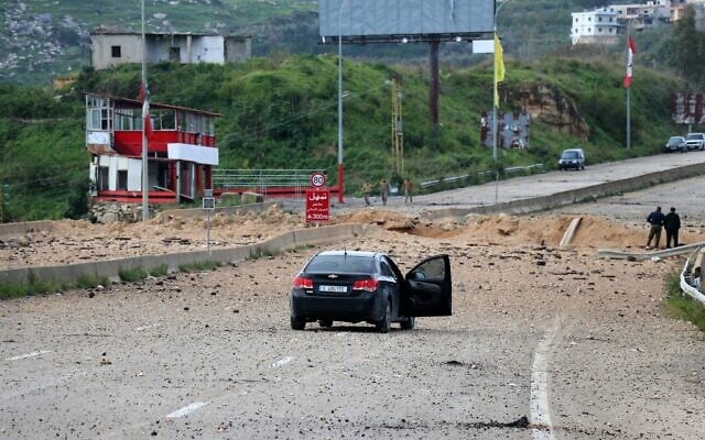 Deux hommes se tiennent près d'un cratère au lendemain d'une frappe aérienne de l'armée israélienne qui a visé le pont de Qasmiyeh, après qu'Israël eut déclaré qu'il était utilisé par le Hezbollah, dans le sud du Liban, le 23 mars 2026 (Crédit : Kawnat HAJU / AFP)
