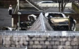 Une femme marche à proximité d'ambulances incendiées (à droite) dans le quartier de Golders Green, dans le nord de Londres, le 23 mars 2026, après l'incendie criminel, pendant la nuit, d'ambulances bénévoles gérées par une organisation juive. (Photo par Henry NICHOLLS / AFP)