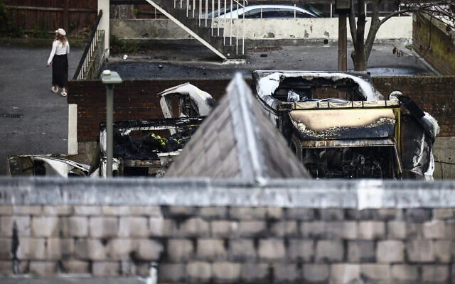 Une femme marche à proximité d'ambulances incendiées (à droite) dans le quartier de Golders Green, dans le nord de Londres, le 23 mars 2026, après l'incendie criminel, pendant la nuit, d'ambulances bénévoles gérées par une organisation juive. (Photo par Henry NICHOLLS / AFP) Une femme marche à proximité d'ambulances incendiées (à droite) dans le quartier de Golders Green, dans le nord de Londres, le 23 mars 2026, après l'incendie criminel, pendant la nuit, d'ambulances bénévoles gérées par une organisation juive. (Photo par Henry NICHOLLS / AFP)
