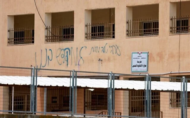 Ce graffiti laissé par des résidents d'implantations juifs, qui dit en substance : « Un bon Arabe est un Arabe mort », recouvre les murs de l’école secondaire palestinienne de Huwara, d'où un drapeau israélien placé sur le toit par des résidents d'implantations israéliens aurait été retiré, remplacé par le drapeau palestinien, à Huwara, dans le sud de Naplouse, en Cisjordanie, le 23 mars 2026.(Jaafar ASHTIYEH / AFP)