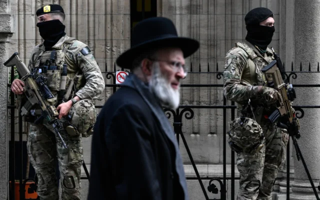 Des militaires belges armés de fusils d'assaut FN SCAR montent la garde devant une synagogue du centre d'Anvers, dans le cadre des mesures de sécurité renforcées mises en place par la Belgique dans les écoles juives et les synagogues, le 23 mars 2026. (Crédit: JOHN THYS / AFP)