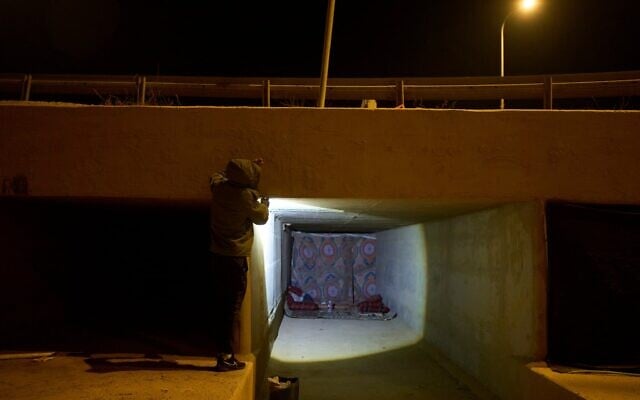 Un Bédouin éclairant avec sa lampe torche l'abri de fortune qu'il partage avec une centaine de membres de sa communauté pour les protéger des tirs iraniens, à proximité d'un canal de drainage près d'Arad, dans le sud d'Israël, le 17 juin 2025. (Crédit : Maya Alleruzzo/AP)