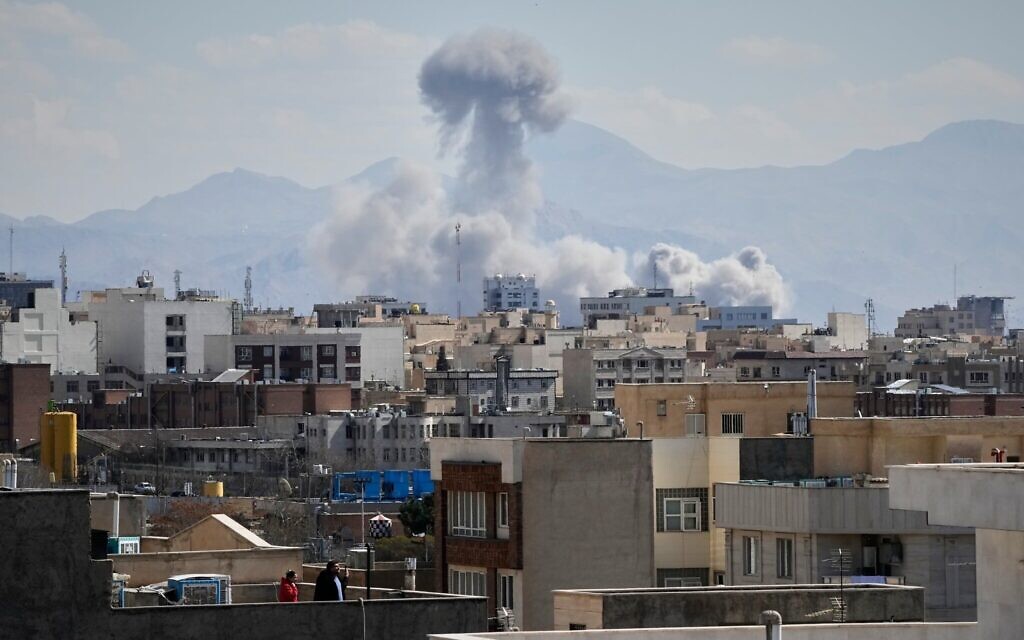 Des personnes observant depuis un toit une colonne de fumée s'élever après une frappe à Téhéran, en Iran, le 1ᵉʳ mars 2026. (Crédit : Vahid Salemi/AP)