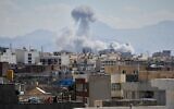 Des personnes observant depuis un toit une colonne de fumée s'élever après une frappe à Téhéran, en Iran, le 1ᵉʳ mars 2026. (Crédit : Vahid Salemi/AP)
