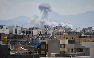 Des personnes observant depuis un toit une colonne de fumée s'élever après une frappe à Téhéran, en Iran, le 1ᵉʳ mars 2026. (Crédit : Vahid Salemi/AP)