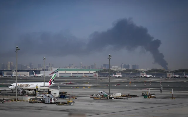 Un panache de fumée causé par une frappe iranienne  au loin alors que des avions Emirates sont stationnés à l’aéroport international de Dubaï, après sa fermeture à Dubaï, aux Émirats arabes unis, le 1ᵉʳ mars 2026. (Crédit : Altaf Qadri/AP)
