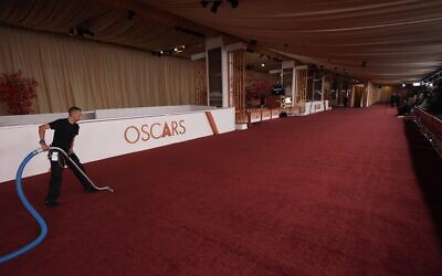 Un homme passant l'aspirateur sur un tapis rouge désert, au Dolby Theatre de Los Angeles, la veille de la 98ᵉ cérémonie des Oscars, le 14 mars 2026. (Crédit : Gregory Bull/AP Photo)