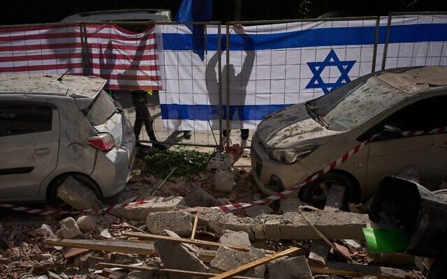 Les autorités israéliennes hissent les drapeaux israélien et américain sur le site touché par un missile iranien qui a fait deux morts, à Ramat Gan, le mercredi 18 mars 2026. (Crédit : AP Photo/Oded Balilty)