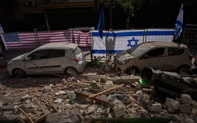 Les autorités israéliennes hissent les drapeaux israélien et américain sur le site touché par un missile iranien qui a fait deux morts, à Ramat Gan, le mercredi 18 mars 2026. (Crédit : AP Photo/Oded Balilty)