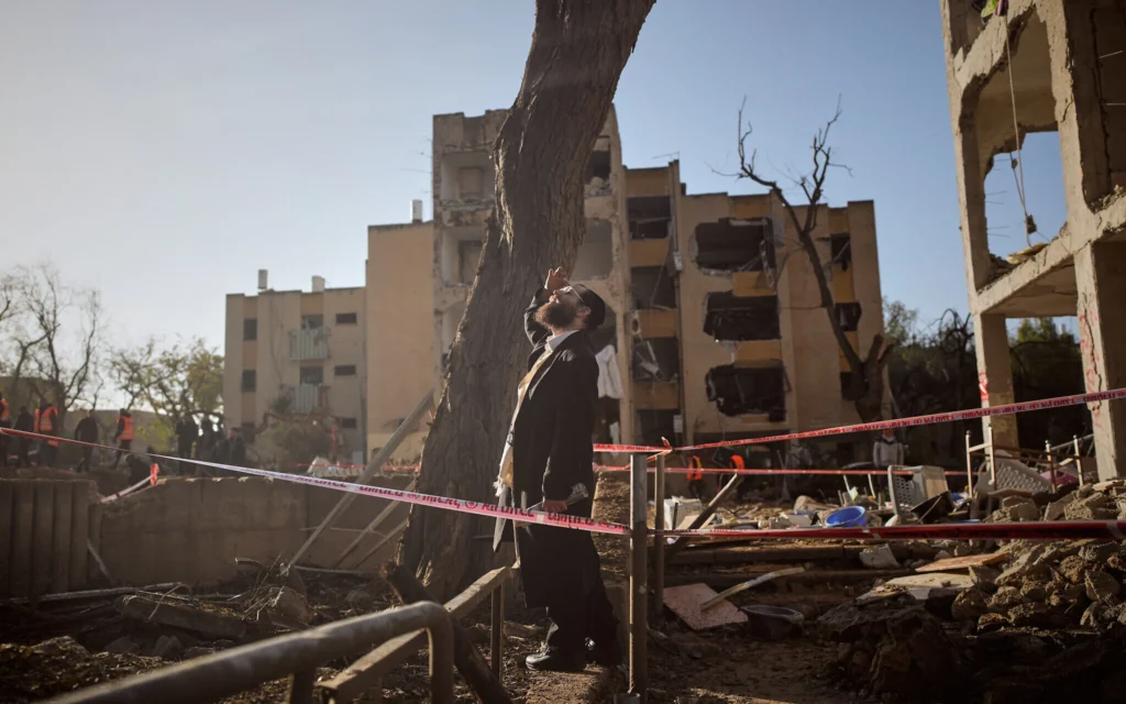 Un homme observe des immeubles d’habitation endommagés par une frappe de missile iranienne dans la ville d’Arad, au sud du pays, le 22 mars 2026. (Crédit : AP Photo/Ohad Zwigenberg)