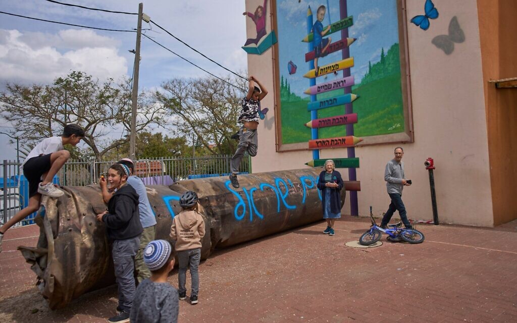 Des enfants jouant à côté d'un fragment de missile balistique iranien sur lequel il est écrit "Le peuple d'Israël vit" qui s'est écrasé dans la cour d'une école de l'implantation de Peduel, en Cisjordanie, le 23 mars 2026. (Crédit : Ohad Zwigenberg/AP Photo) Des enfants jouant à côté d'un fragment de missile balistique iranien sur lequel il est écrit "Le peuple d'Israël vit" qui s'est écrasé dans la cour d'une école de l'implantation de Peduel, en Cisjordanie, le 23 mars 2026. (Crédit : Ohad Zwigenberg/AP Photo)