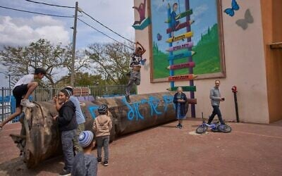 Des enfants jouant à côté d'un fragment de missile balistique iranien sur lequel il est écrit "Le peuple d'Israël vit" qui s'est écrasé dans la cour d'une école de l'implantation de Peduel, en Cisjordanie, le 23 mars 2026. (Crédit : Ohad Zwigenberg/AP Photo)