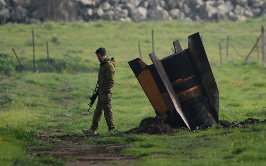Un soldat israélien se tenant à côté d’un fragment de missile tiré depuis l’Iran et intercepté par le système de défense aérienne israélien, encastré dans un champ à ciel ouvert sur le plateau du Golan, le 19 mars 2026. (Crédit : Ohad Zwigenberg/AP)
