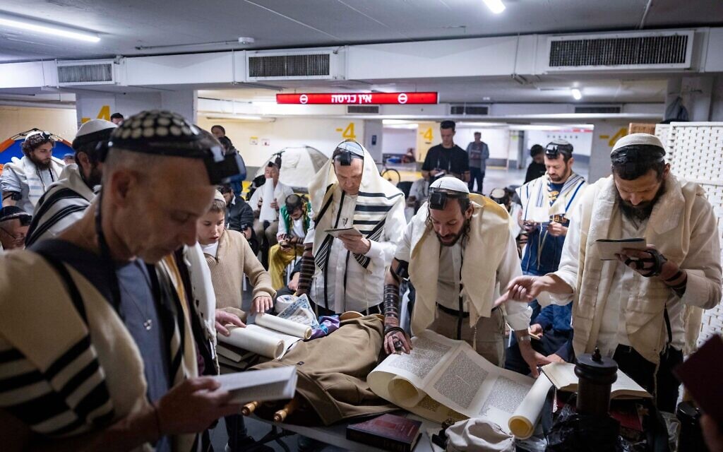Des personnes lisent le rouleau d'Esther lors de la fête de Pourim dans un parking souterrain transformé en abri à Tel-Aviv, en pleine guerre avec l'Iran et sous les tirs de missiles incessants vers Israël, le 3 mars 2026. (Crédit : Chaim Goldberg/Flash90)