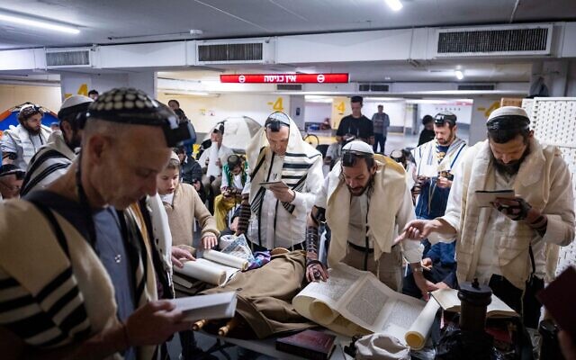Des personnes lisent le rouleau d'Esther lors de la fête de Pourim dans un parking souterrain transformé en abri à Tel-Aviv, en pleine guerre avec l'Iran et sous les tirs de missiles incessants vers Israël, le 3 mars 2026. (Crédit : Chaim Goldberg/Flash90)