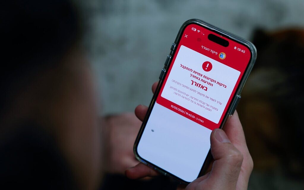 Un homme montrant une notification d’alerte de missile sur son téléphone portable alors que les habitants se mettent à l’abri suite à un tir de missiles depuis l’Iran vers Israël, à Mishmar David, le 10 mars 2026. (Crédit : Nati Shohat/Flash90)