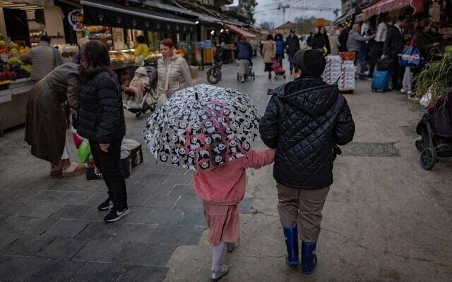 Des passants marchant sous la pluie au marché Mahane Yehuda, à Jérusalem, le 24 mars 2026. (Crédit : Yonatan Sindel/Flash90)