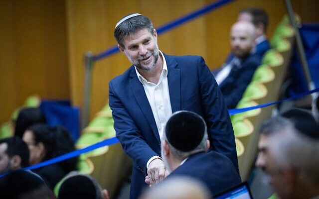 Le ministre des Finances Bezalel Smotrich serre la main du chef du Shas, Aryeh Deri (dos à la caméra), lors du vote sur l'adoption du budget de l'État à la Knesset, tôt dans la matinée du 30 mars 2026. La séance s'est tenue dans une salle sécurisée en raison de la guerre en cours avec l'Iran. (Crédit : Yonatan Sindel/Flash90)