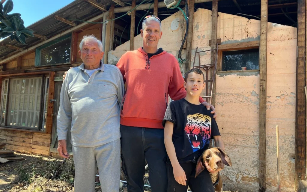 Yonatan Schwartz, à gauche, avec Yaniv, Tsur et leur chien Lev, devant leur restaurant à Moshav Liman, endommagé lors du conflit de 2024 avec le Hezbollah, le 10 mars 2026. (Crédit : Diana Bletter/Times of Israel)