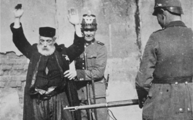 La police allemande fouille un homme juif âgé sous la menace d'une arme à Kolo, en Pologne, vers 1941. (Avec l'aimable autorisation du United States Holocaust Memorial Museum / Instytut Pamieci Narodowej)