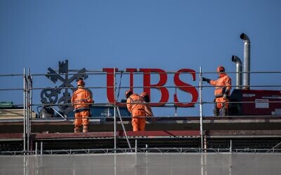 Des ouvriers travaillent près d'une enseigne du géant bancaire suisse UBS, au sommet d'un immeuble à Zurich, le 4 mars 2026. (Crédit : Fabrice COFFRINI / AFP)