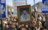 Un partisan des Houthis du Yémen tient une photo de leur chef Abdul-Malik al-Houthi alors que d'autres brandissent leurs armes tout en se mobilisant en solidarité avec l'Iran et le Hezbollah libanais, dans le cadre de la guerre américano-israélienne contre l'Iran à Sanaa, la capitale du Yémen, le 27 mars 2026. (Mohammed Huwais/AFP)