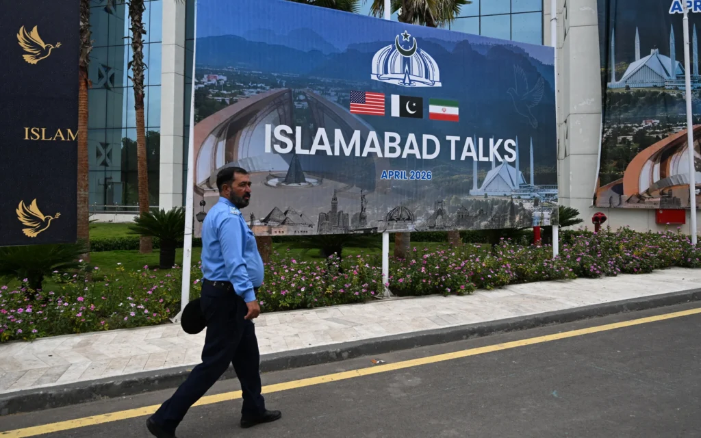 Un policier passant devant un panneau d'affichage annonçant les pourparlers entre les États-Unis et l'Iran, à Islamabad, le 11 avril 2026 (Crédit : Amir Qureshi/AFP)