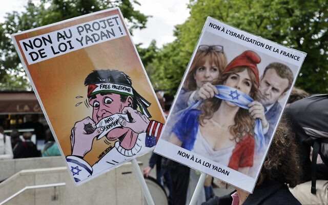 Une manifestante brandit des pancartes « Non à la loi Yadan » et « non à l'israélisation de la France » lors d'un rassemblement devant l'Assemblée nationale, la chambre basse du Parlement français, à Paris, le 16 avril 2026, contre le projet de loi Yadan, visant à lutter contre les « nouvelles formes » d'antisémitisme. (Crédit : Stéphane de Sakutin / AFP)