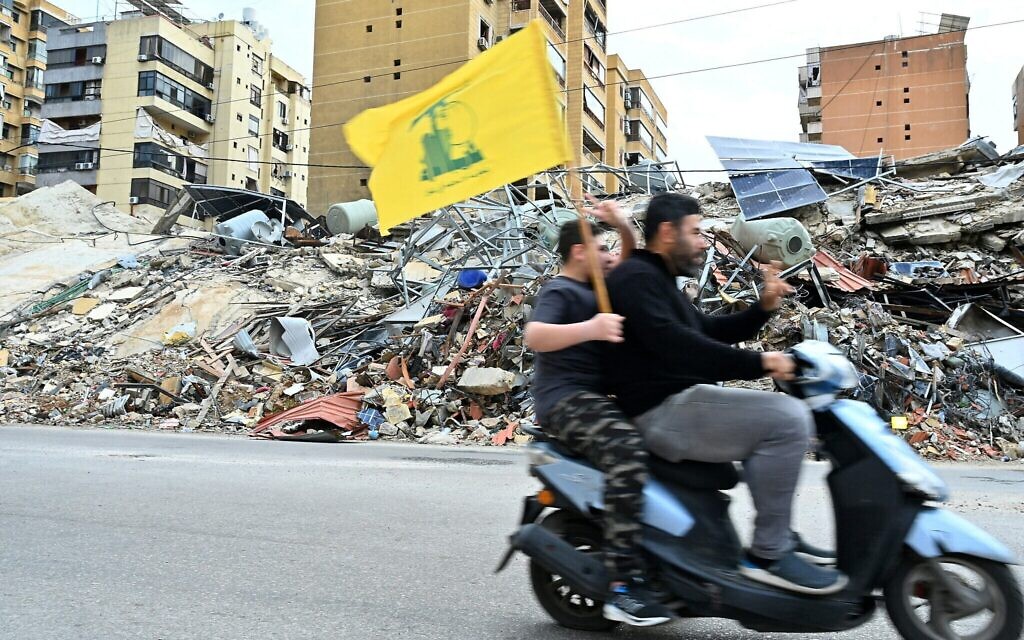 Des partisans du Hezbollah brandissent le drapeau du groupe terroriste chiite libanais soutenu par l'Iran alors qu'ils passent à moto devant les dégâts causés par les combats, à leur retour dans leur quartier de la banlieue sud de Beyrouth, après l'entrée en vigueur d'un cessez-le-feu de dix jours avec Israël, le 17 avril 2026. (Crédit : Fadel Itani/AFP)