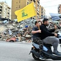 Des partisans du Hezbollah brandissent le drapeau du groupe terroriste chiite libanais soutenu par l'Iran alors qu'ils passent à moto devant les dégâts causés par les combats, à leur retour dans leur quartier de la banlieue sud de Beyrouth, après l'entrée en vigueur d'un cessez-le-feu de dix jours avec Israël, le 17 avril 2026. (Crédit : Fadel Itani/AFP)