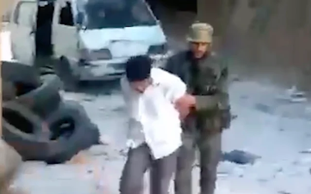 Capture d’écran d’une vidéo montrant un Syrien aux yeux bandés poussé par un agent syrien avant d’être abattu et jeté dans une grande fosse remplie de cadavres dans le quartier de Tadamon à Damas, en Syrie. (Crédit : AP)