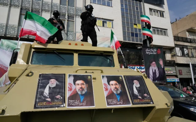 Des policiers se tiennent debout sur le toit de leur voiture, tenant des photos du défunt Guide suprême iranien, l'ayatollah Ali Khamenei (à droite et à gauche), et de son fils et successeur, l'ayatollah Mojtaba Khamenei, lors d'un rassemblement à Téhéran, en Iran, le 9 mars 2026. (Crédit : AP/Vahid Salemi)