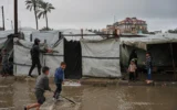 Des enfants palestiniens déplacés traversent un campement de tentes détrempé par la pluie après de fortes précipitations à Deir al-Balah, dans le centre de la bande de Gaza, le jeudi 26 mars 2026. (. (Crédit : AP/Abdel Kareem Hana)