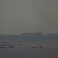 Des bateaux de pêche parsemant la mer tandis que, en arrière-plan, des cargos traversent le golfe Persique en direction du détroit d'Ormuz, au large des Émirats arabes unis, le 27 mars 2026. (Crédit : AP)