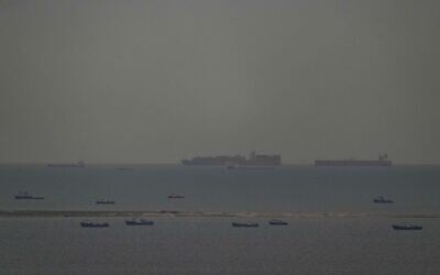 Des bateaux de pêche parsemant la mer tandis que, en arrière-plan, des cargos traversent le golfe Persique en direction du détroit d'Ormuz, au large des Émirats arabes unis, le 27 mars 2026. (Crédit : AP)