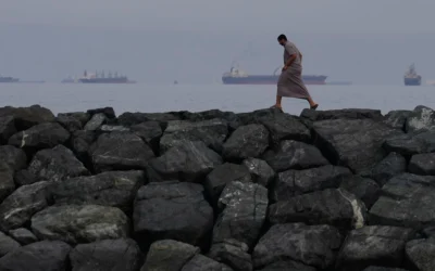 Un homme marche le long du rivage tandis que des pétroliers et des cargos s'alignent dans le détroit d'Ormuz, vu depuis Khor Fakkan, aux Émirats arabes unis, le 11 mars 2026. (Crédit : AP Photo/Altaf Qadri)