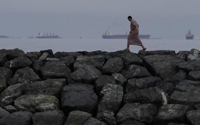 Un homme marchant le long du rivage tandis que des pétroliers et des cargos s’alignent dans le détroit d’Ormuz, vu depuis Khor Fakkan, aux Émirats arabes unis, le 11 mars 2026. (Crédit : Altaf Qadri/AP Photo) Un homme marchant le long du rivage tandis que des pétroliers et des cargos s’alignent dans le détroit d’Ormuz, vu depuis Khor Fakkan, aux Émirats arabes unis, le 11 mars 2026. (Crédit : Altaf Qadri/AP Photo)