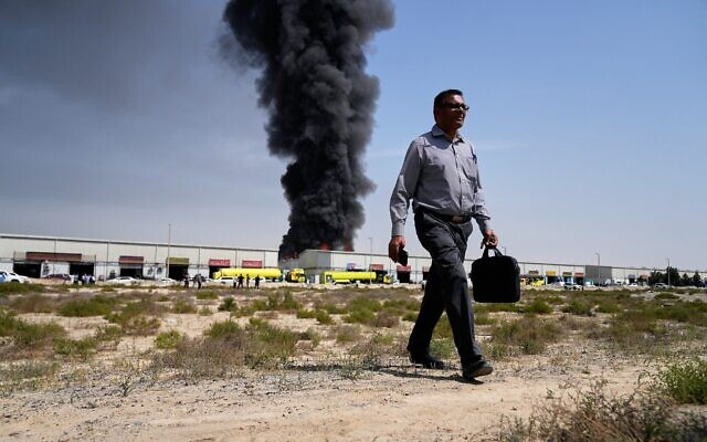 Illustration : Un homme s’éloignant d'un panache de fumée noire s’élevant d’un entrepôt ,dans la zone industrielle de la ville de Sharjah, aux Émirats arabes unis, à la suite d’une frappe iranienne, le 1ᵉʳ mars 2026. (Crédit : Altaf Qadri/AP Photo)